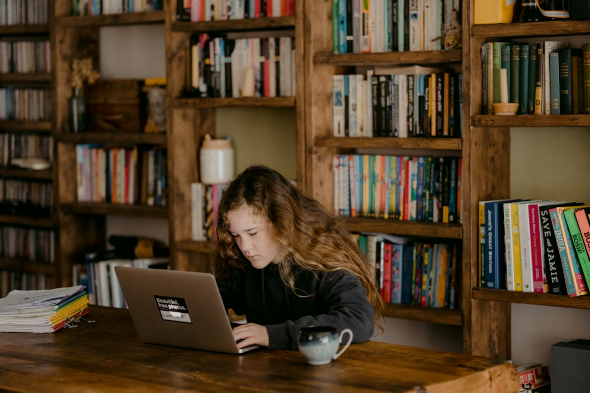 Young teen doing schoolwork at home by reading online on a laptop