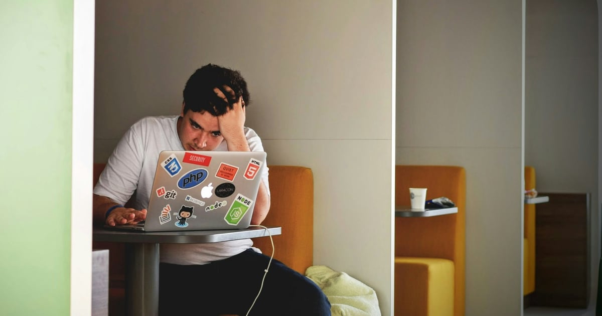Frustrated developer resting head in hand in front of a sticker-covered laptop