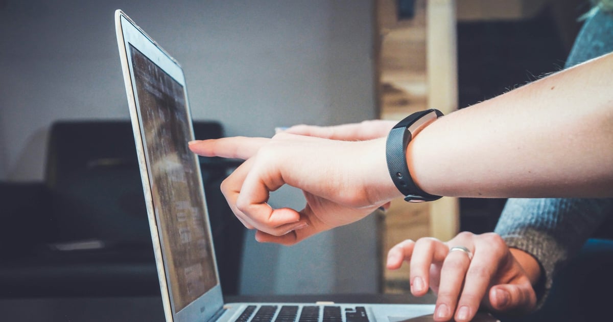 Two people collaborating at a laptop, with one person pointing at the screen.