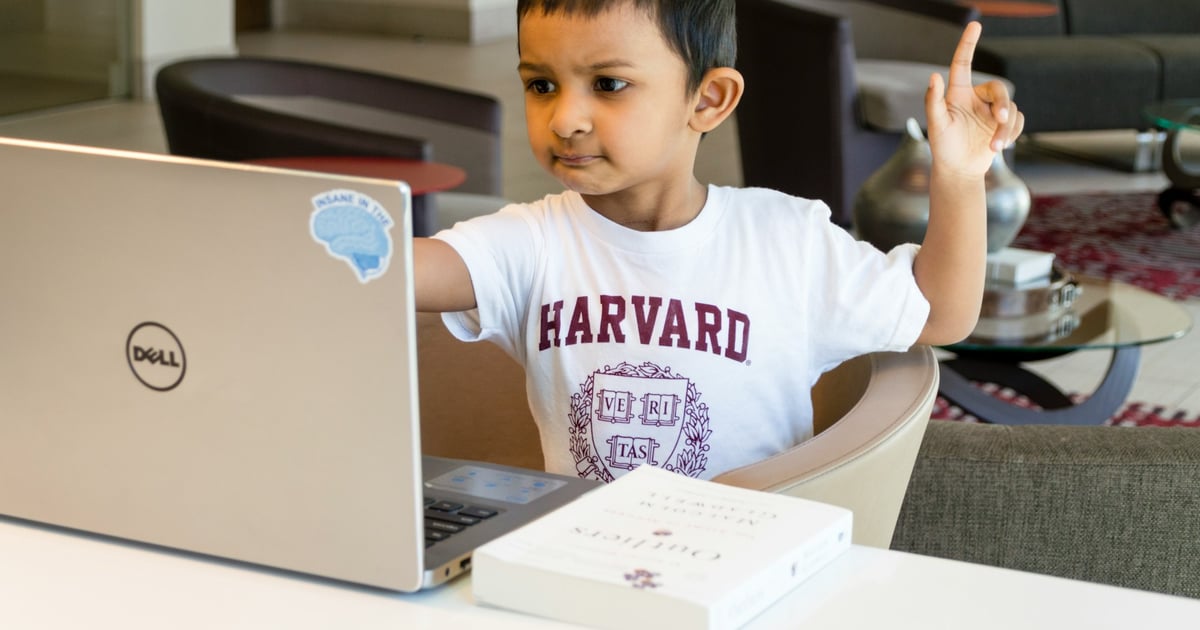Young boy in front of laptop raising his hand.