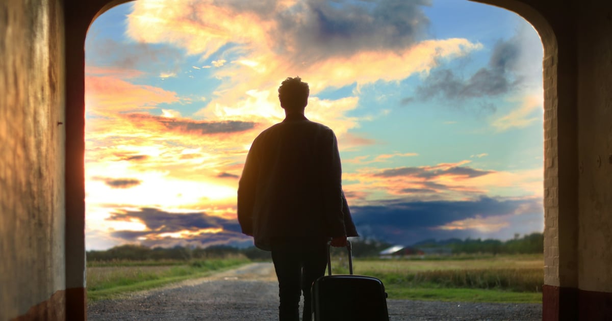 Man with suitcase going through door with nice sky in background