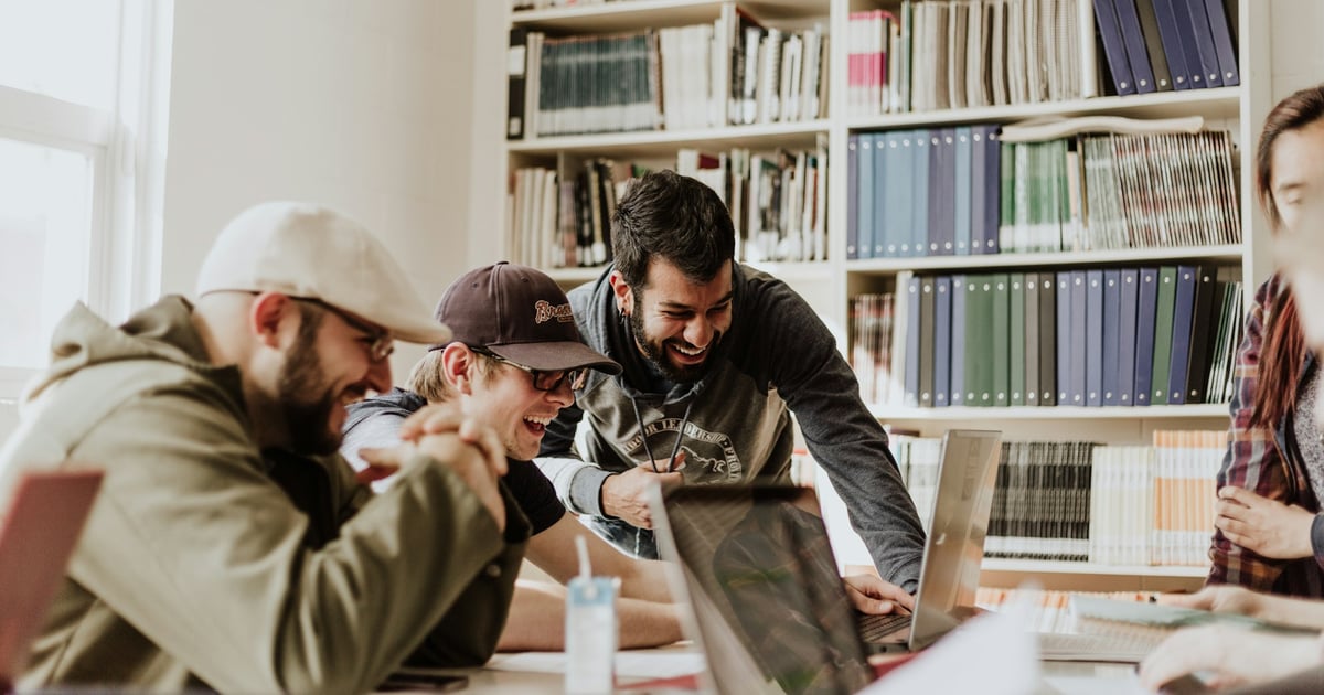 Group of friends laughing and looking at a laptop together in a library.