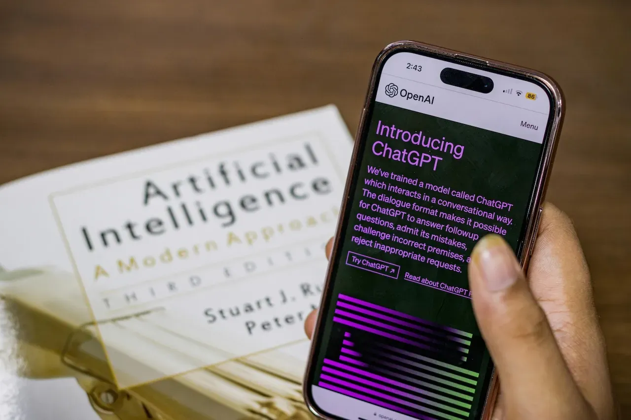 Free Close-up of a smartphone displaying ChatGPT app held over AI textbook.